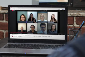 Imagem Acessível: A imagem mostra um homem sentada à mesa assistindo, em um notebook, a uma live no YouTube com oito participantes em janelas de vídeo. O título da transmissão é “Reforma Administrativa e PEC 66: ameaças e desafios”. No rodapé da imagem, em destaque, está o texto: “SINJUS denuncia riscos contidos na Reforma Administrativa e na PEC 66”.