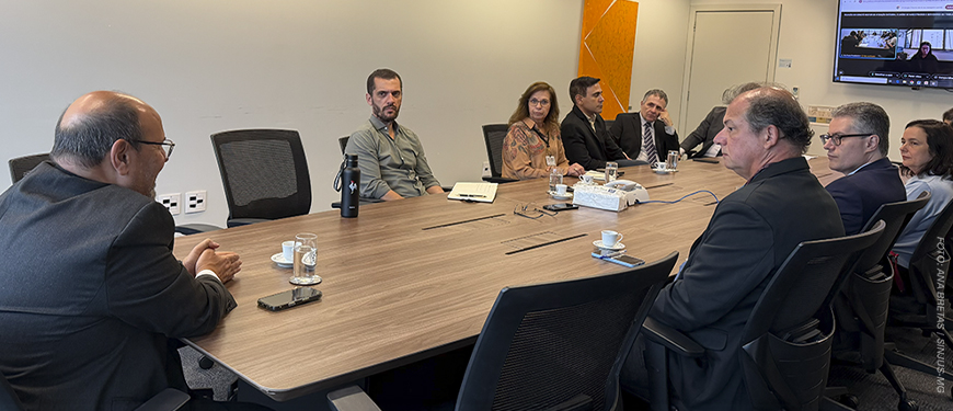 Imagem acessível: A imagem mostra uma reunião do Comitê Gestor de Atenção Integral à Saúde de Magistrados e Servidores do TJMG, com representantes reunidos em torno de uma mesa. No centro da arte, o título “Comitê debate ações de saúde e SINJUS cobra melhorias nas condições de trabalho do TJMG”. Na base da imagem, aparece o logo do SINJUS-MG.