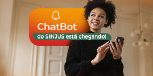 A imagem anuncia a chegada do ChatBot do SINJUS. Em destaque, aparece uma mulher sorridente segurando um celular, simbolizando praticidade e acesso digital. O texto tem o aviso: “O ChatBot do SINJUS está chegando!”, destacando a novidade como um recurso de atendimento contínuo aos filiados.