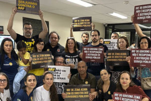 A imagem mostra um grupo de pessoas reunidas, segurando cartazes e protestando