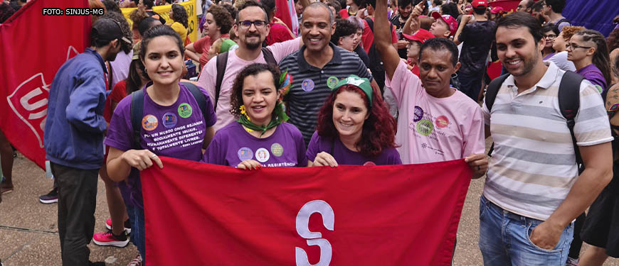 Diretores do SINJUS posam junto de manifestantes com a bandeira do Sindicato, aparecem na imagem: Adriana Teodoro, diretora de Assuntos Sociais e Saúde, Alexandre Gomes, diretor de Imprensa e Comunicação, Wagner Ferreira, diretor de Assuntos Jurídicos e vereador de BH, e Jonas Pinheiro, diretor de Formação Política.