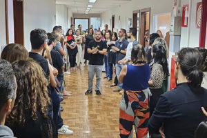 Fotografia da parte interna do Èdificio Afonso Pena 1500 onde aparecem os diretores do Sinjus em um corredor com chão de madeira, paredes brancas, eles estão dialogando com os servidores, o ambiente é de atenção.