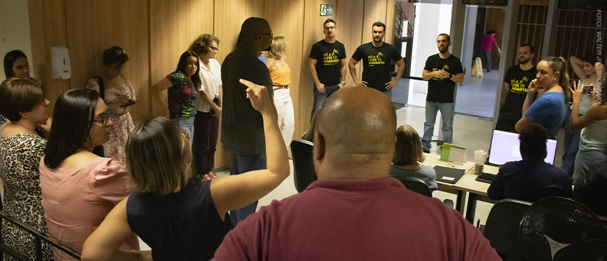 A imagem mostra os servidores em roda em um corredor da unidade Afonso Pena 1.500 do TJMG, enquanto os dirigentes sindicais Alexandre Pires, Janaína Torres, Felipe Tomanini, Felipe Rodrigues e Alexandre Gomes ouvem um relado de uma servidora que gesticula.