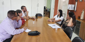A imagem mostra uma sala de reuniões simples, onde cinco pessoas estão sentadas ao redor de uma mesa de madeira, conversando durante uma visita técnica ao Centro Odontológico do Ipsemg, em Belo Horizonte. À direita, duas gestoras da unidade ouvem representantes do Conselho de Beneficiários do Ipsemg (CBI), entre eles o coordenador-geral do SINJUS-MG, Alexandre Pires.