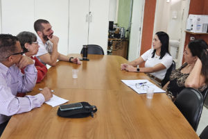A imagem mostra uma sala de reuniões simples, onde cinco pessoas estão sentadas ao redor de uma mesa de madeira, conversando durante uma visita técnica ao Centro Odontológico do Ipsemg, em Belo Horizonte. À direita, duas gestoras da unidade ouvem representantes do Conselho de Beneficiários do Ipsemg (CBI), entre eles o coordenador-geral do SINJUS-MG, Alexandre Pires.