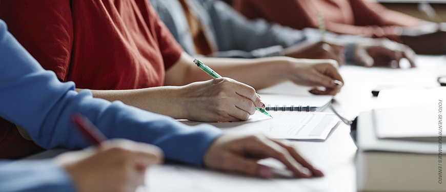A imagem mostra uma fileira de estudantes sentados em sala de aula, escrevendo em cadernos e fazendo anotações. O foco está nas mãos de uma pessoa escrevendo com caneta. Sobre a imagem, o texto diz: “EJEF e PUC Minas firmam parceria para implantação de mestrado e doutorado no TJMG”. No canto superior esquerdo, está o título “Oportunidade” e, no canto inferior, o logotipo do SINJUS-MG.