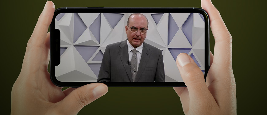 mãos seguram um smartphone, na tela do equipamento aparece a imagem do presidente do TJMG, Des. José Arthur Filho, em anúncio feito por vídeo.