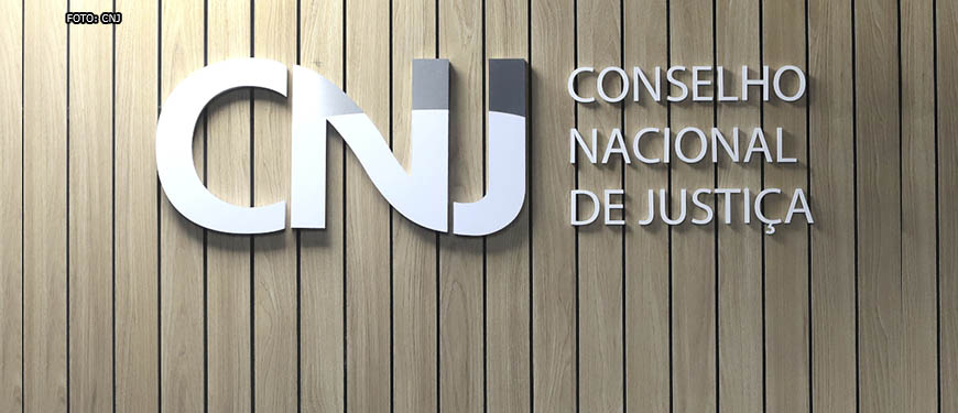 Letreiro em inox do CNJ (Conselho Nacional de Justiça) sobre fundo de madeira.