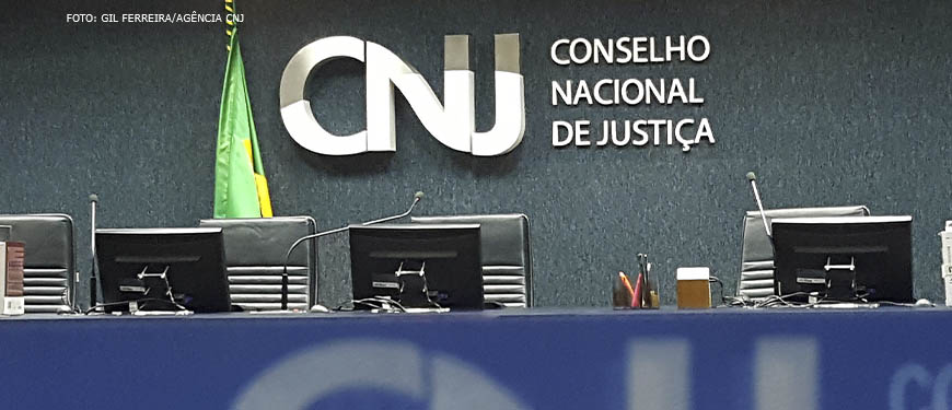 Mesa diretiva do plenário do CNJ, em destaque está o letreiro em aço inox onde se lê a "CNJ - Conselho Nacional de Justiça".
