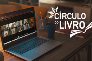 Imagem acessível: A arte apresenta o título “Círculo do Livro aborda pertencimento e valorização da singularidade” sobre a imagem de uma mesa em ambiente acolhedor, com um notebook exibindo uma reunião virtual com diversos participantes. Ao redor aparecem luminária, caneca, lápis, livro e fones de ouvido. A peça identifica a atividade “Mulheres que Correm com os Lobos”, traz a marca do Círculo do Livro e o símbolo do SINJUS na parte inferior.