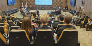 Sessão do Órgão Especial do Tribunal de Justiça de Minas Gerais (TJMG) em auditório. Público visto de costas e membros do Tribunal na frente, com tela de projeção de pautas