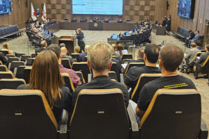 Sessão do Órgão Especial do Tribunal de Justiça de Minas Gerais (TJMG) em auditório. Público visto de costas e membros do Tribunal na frente, com tela de projeção de pautas