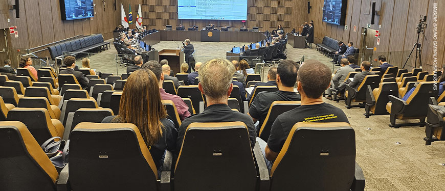 Sessão do Órgão Especial do Tribunal de Justiça de Minas Gerais (TJMG) em auditório. Público visto de costas e membros do Tribunal na frente, com tela de projeção de pautas