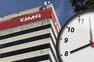 A imagem mostra a fachada do prédio do TJMG vista de baixo para cima, com um grande relógio marcando oito horas em primeiro plano simbolizando o debate sobre a jornada de trabalho. No topo lê-se “Intransigência”.