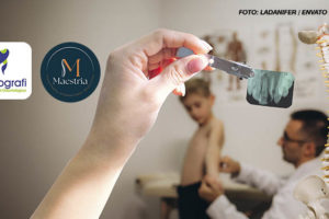 A imagem mostra um consultório médico onde um profissional da saúde em quiropraxia , que aparentemente é médico ou fisioterapeuta, está examinando um menino sem camisa. Em primeiro plano, há um modelo anatômico de uma coluna vertebral em cima de uma mesa ao lado se vê uma montagem digital de um braço segurando um raio x por prendedor metálico. Ao fundo, pode-se ver cartazes com ilustrações do corpo humano na parede. O profissional está de óculos e parece estar focado na avaliação do paciente.