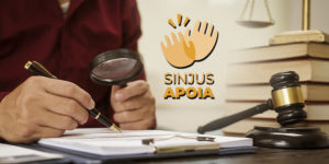 A arte mostra ao fundo uma foto de uma pessoa analisando documentos com uma lupa, ao lado de um martelo de juiz, livros e uma balança da Justiça.