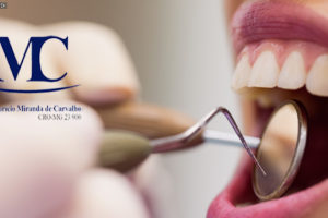 Em destaque, mão de dentista durante atendimento segurando um espelho e uma pinça perto de uma boca aberta de paciente. Na imagem tem a logo do dentista Maurício Miranda de Carvalho (CRO-MG 23.900).