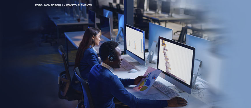 Imagem Acessível: Há duas pessoas, um homem negro e uma mulher branca em trajes sociais em frente ao computador. O ambiente está escuro, iluminado somente pelo monitor, há vários computadores em bancadas com cadeiras vazias em frente. Conteúdo textual: Plantão de habeas corpus - TJMG realiza pagamentos apenas para plantões realizados até 2023 e sindicatos criticam falta de transparência.