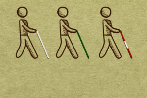 A imagem mostra três figuras estilizadas de uma pessoa utilizando diferentes tipos de bengala para deficientes visuais. O desenho das figuras sugere a ação de caminhar, destacando o uso dessas bengalas como auxílio à mobilidade. Todas as figuras são desenhadas com linhas simples em marrom sobre um fundo verde texturizado. A primeira figura, à esquerda, segura uma bengala branca. A segunda figura, no centro, segura uma bengala verde. A terceira figura, à direita, segura uma bengala com faixas vermelhas e brancas. Conteúdo textual: Nova lei - Entenda as diferenças entre as bengalas brancas, verdes e vermelhas.