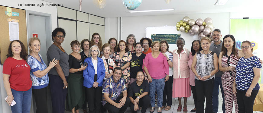 Foto das pessoas presentes na confraternização do Núcleo dos aposentados e pensionistas aplicado em cima de um fundo verde com decorações de natal.