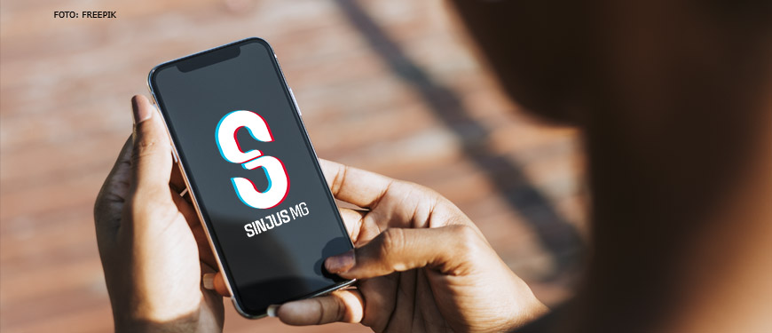 Foto/imagem de uma pessoa segurando um celular, na tela do mesmo se vê o logo do SINJUS-MG.