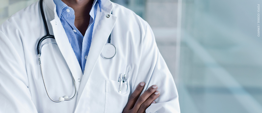 A imagem mostra ao fundo a foto do tronco de um profissional de saúde, vestindo jaleco branco com um estetoscópio pendurado no pescoço e os braços cruzados. No topo, lê-se “Déficit de servidores” e, em destaque ao centro, o texto diz: “Sindicatos reiteram solicitação de nomeação de médico para Polo de Saúde de Poços de Caldas”. Na parte inferior, aparece o símbolo do SINJUS.