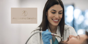 Imagem Acessível: Dentista jovem, de cabelos lisos e castanhos, sorri enquanto atende um paciente deitado na cadeira odontológica. Ela usa jaleco branco e luvas azuis. No canto esquerdo da imagem, há o logotipo “Ana Carolina Carvalho Odontologia”. Sobreposto à foto, está o texto: “Garanta saúde bucal e estética com o novo convênio do SINJUS”.