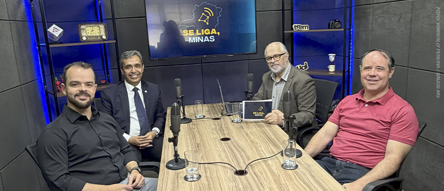 Imagem acessível: A imagem mostra o registro fotográfico do último episódio do podcast Se Liga, Minas. Em destaque, o título diz: "Legado de JK atravessa gerações e inspira debate no Se Liga, Minas". Na base da imagem, aparece a logomarca do SINJUS-MG.