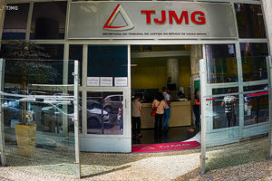 Fachada da Unidade Goiás do TJMG, com placa em aço inox com a marca do Tribunal e letreiro com a identificação do local "Secretaria do Tribunal de Justiça de Minas Gerais" .