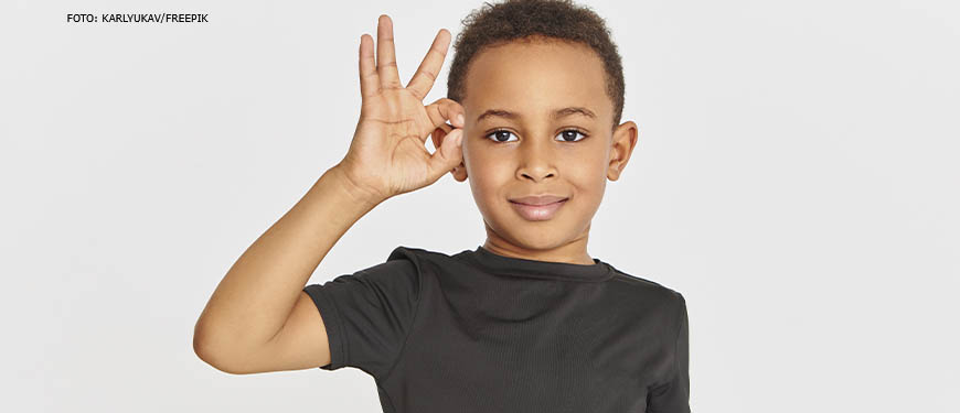 Menino negro faz um gesto de aprovação na língua de sinais e sorri.