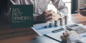 Imagem Acessível: A imagem mostra duas pessoas em reunião sobre finanças, com gráficos, calculadora e pilhas de moedas sobre a mesa. No canto inferior esquerdo, aparece o logo da consultoria ‘Seu Rico Dinheiro’, com a imagem de um cofrinho. Sobre a imagem, lê-se o texto: ‘Transforme sua relação com o dinheiro com a nova parceria do SINJUS’.