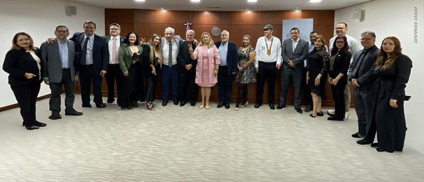 Grupo de pessoas integrantes de uma comitiva posam para foto em uma sala institucional durante visita oficial a autoridades do Paraguai. Todos estão alinhados em pé, formando uma fileira, vestidos de maneira formal, com painel de madeira e brasão ao fundo.