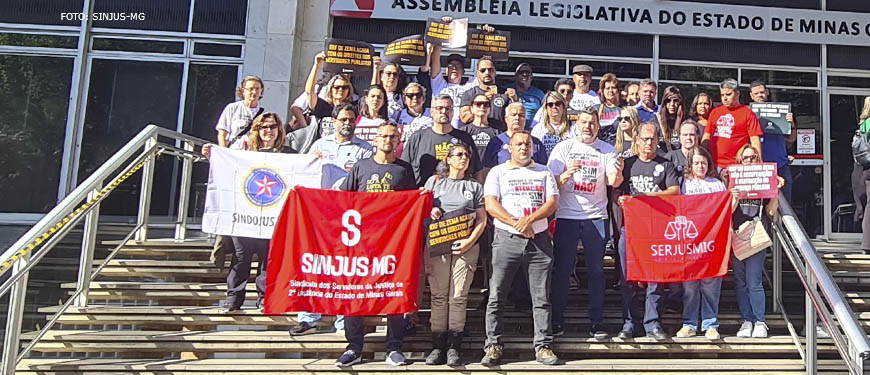 Grupo de representantes do Serjusmig, SINDOJUS/MG e SINJUS-MG, reunidos para foto em frente à entrada da ALMG, eles carregam bandeiras dos três sindicatos e cartazes em protesto contra o RRF do Governo Zema (Regime de Recuperação Fiscal). Entre os sindicalistas está o diretor de Imprensa e Comunicação do SINJUS-MG, Alexandre Gomes.