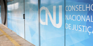 A imagem mostra a fachada do Conselho Nacional de Justiça (CNJ), com sua identidade visual em tons de azul e branco, onde está escrito “Conselho Nacional de Justiça”. O texto sobreposto indica: “Fenajud denuncia tentativa de esvaziamento da Resolução 219 por parte do Conselho de Presidentes de Tribunais”. A manchete em destaque usa cores contrastantes (amarelo e branco sobre fundo escuro).
