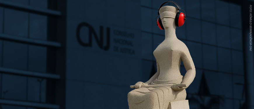 Escultura da Justiça em frente ao prédio do Conselho Nacional de Justiça (CNJ), com o fundo desfocado mostrando o logotipo da instituição. A escultura, representando uma figura feminina de olhos vendados e sentada com uma espada no colo, aparece editada com fones de ouvido vermelhos de proteção acústica, sugerindo uma crítica visual à surdez institucional. Foto original por Romulo Serpa/Agência CNJ.