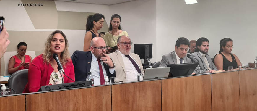 a mesa diretiva da votação da CAP (Comissão de Administração Pública da ALMG) com deputados reunidos, em destaque está a deputada Beatriz Cerqueira, uma mulher branca e loira, vestida em traje vermelho.