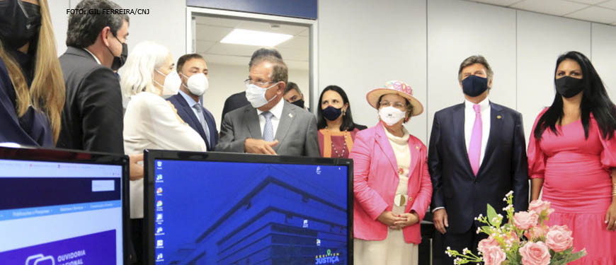 Foto de homens e mulheres brancos, em trajes sociais, reunidos na inauguração da Ouvidoria Nacional da Mulher, em uma sala com computadores. Em destaque, estão a ouvidora nacional da Mulher, Tânia Regina Silva Reckziegel, o presidente do CNJ, ministro Luiz Fux, e o presidente do Superior Tribunal de Justiça (STJ), ministro Humberto Martins.Conteúdo textual: Proteção – CNJ inaugura Ouvidoria Nacional da Mulher.