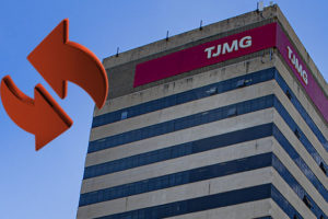 Imagem Acessível: Imagem em formato vertical de um prédio institucional alto, visto de baixo para cima, contra um céu azul limpo. No topo da edificação, há uma faixa vermelha com a sigla “TJMG” em destaque. A fachada é composta por faixas horizontais claras intercaladas com janelas escuras espelhadas. Na base da imagem, aparecem árvores verdes e alguns fios elétricos, indicando que a foto foi feita em área urbana. À direita da imagem, há um elemento gráfico em vermelho com duas setas curvas, sugerindo movimento ou troca. Conteúdo textual: LOTAÇÃO - TJMG convoca servidores classificados no Edital de Remoção nº 01/2025.