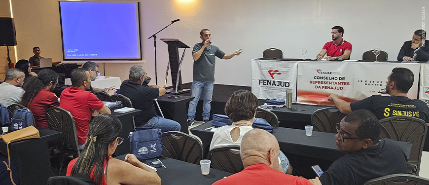 A imagem retrata um auditório com servidoras e servidores sentados em fileiras, acompanhando um encontro sindical. Ao centro, o coordenador-geral do SINJUS e coordenador de Assuntos Jurídicos da Fenajud, Alexandre Pires, fala ao microfone e gesticula para o público. Há uma tela de projeção à esquerda e elementos gráficos sobrepostos destacando a temática da articulação nacional, além da marca do SINJUS-MG na parte inferior.