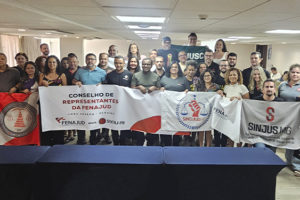 A imagem mostra um grupo numeroso de representantes sindicais posando para foto coletiva durante o Conselho de Representantes da Fenajud. Várias pessoas seguram faixas e bandeiras de seus sindicatos, incluindo o SINJUS-MG.