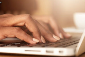 Enquadramento fechado que mostra apenas as mãos de uma pessoa digitando em um teclado de notebook.