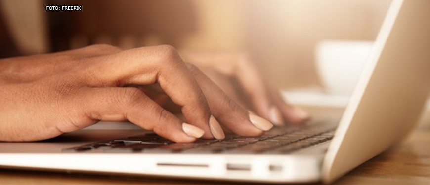 Enquadramento fechado que mostra apenas as mãos de uma pessoa digitando em um teclado de notebook.