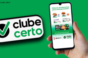 Imagem com fundo ver, sob ela se vê uma mão segurando um celular, na tela do mesmo aparecem propagandas do Clube Certo, ao lado vê se a logo do Clube Certo