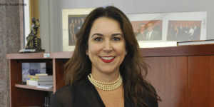 Fotografia da candidata à Presidência do TJMG, Áurea Brasil (mulher de pele clara, cabelos castanhos longos sorrindo e usando batom vermelho, colar de pérolas e blusa preta).