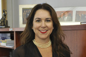 Fotografia da candidata à Presidência do TJMG, Áurea Brasil (mulher de pele clara, cabelos castanhos longos sorrindo e usando batom vermelho, colar de pérolas e blusa preta).