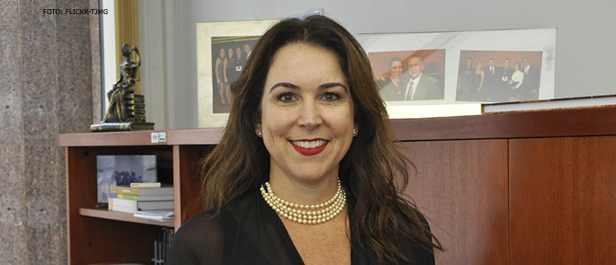 Fotografia da candidata à Presidência do TJMG, Áurea Brasil (mulher de pele clara, cabelos castanhos longos sorrindo e usando batom vermelho, colar de pérolas e blusa preta).