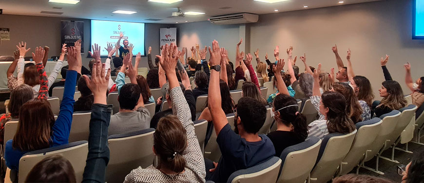 Auditório repleto de pessoas com braços erguidos votando pela aprovação da Pauta de Reivindicações.