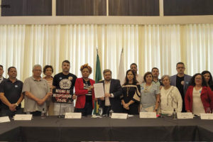 Posicionados atrás de uma grande mesa, lideranças sindicais e o presidente da ALMG, deputado Agostinho Patrus, posam para foto segurando o documento elaborado por entidades representantes dos servidores públicos mineiros.