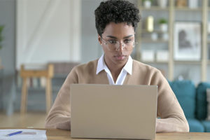 Vídeo de uma mulher de pele negra, cabelos curtos e cacheados, usando óculos de grau enquanto digita em um notebook.