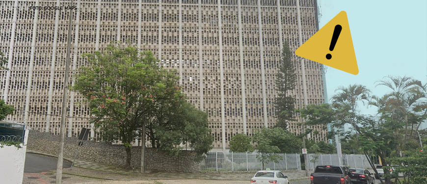 Foto diurna da fachada lateral do edifício situado à Praça Milton Campos, feita de baixo para cima. Sobre ela, é aplicada a figura de uma placa de atenção indicando alerta.